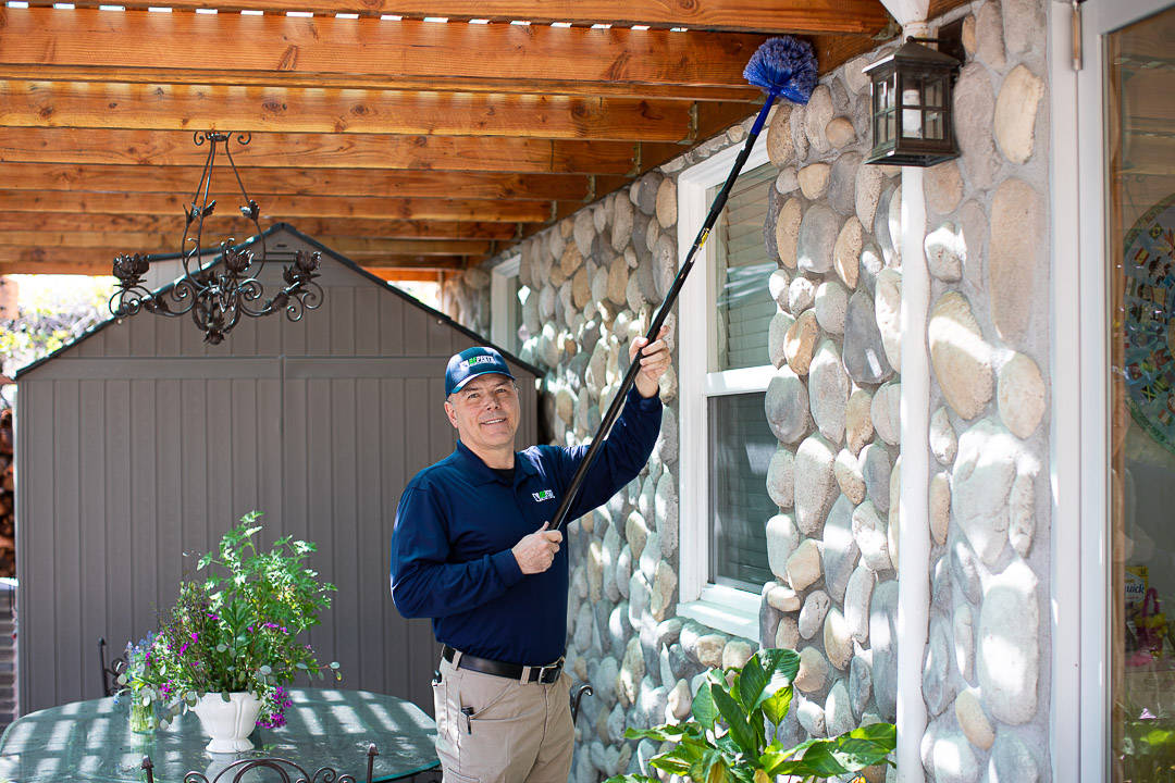 DePests technician treating home exterior eaves for spiders and pests